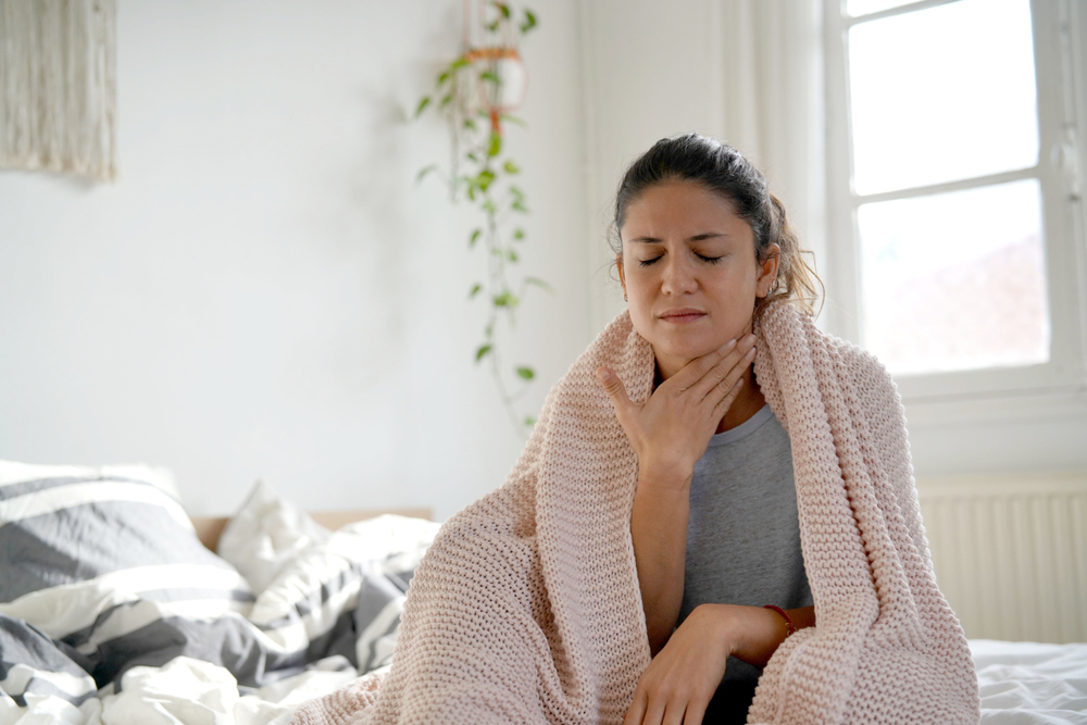 brunette woman sitting on bed with sore throat.
